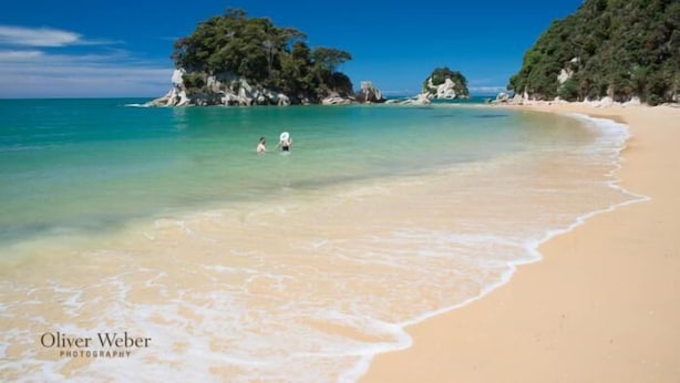 A beach with clear turquoise water, sandy shore, and rocky outcrops.