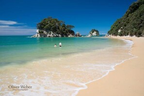 Une plage dotée d’une eau turquoise et limpide, d’un rivage sablonneux et de formations rocheuses.