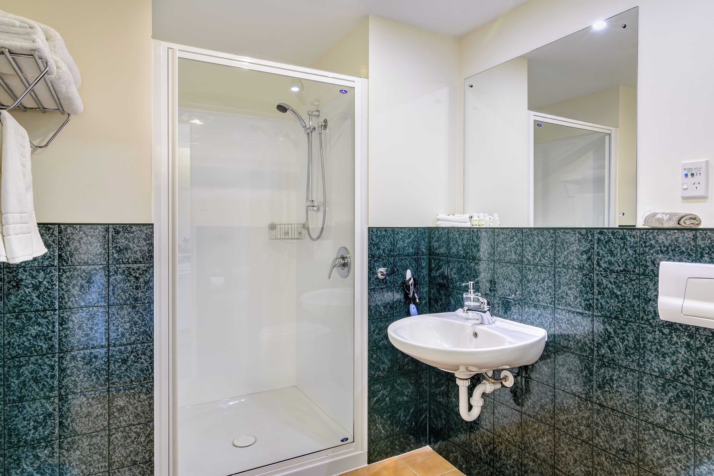 A modern bathroom with a glass-enclosed shower, a white sink, and a marble-tiled wall.