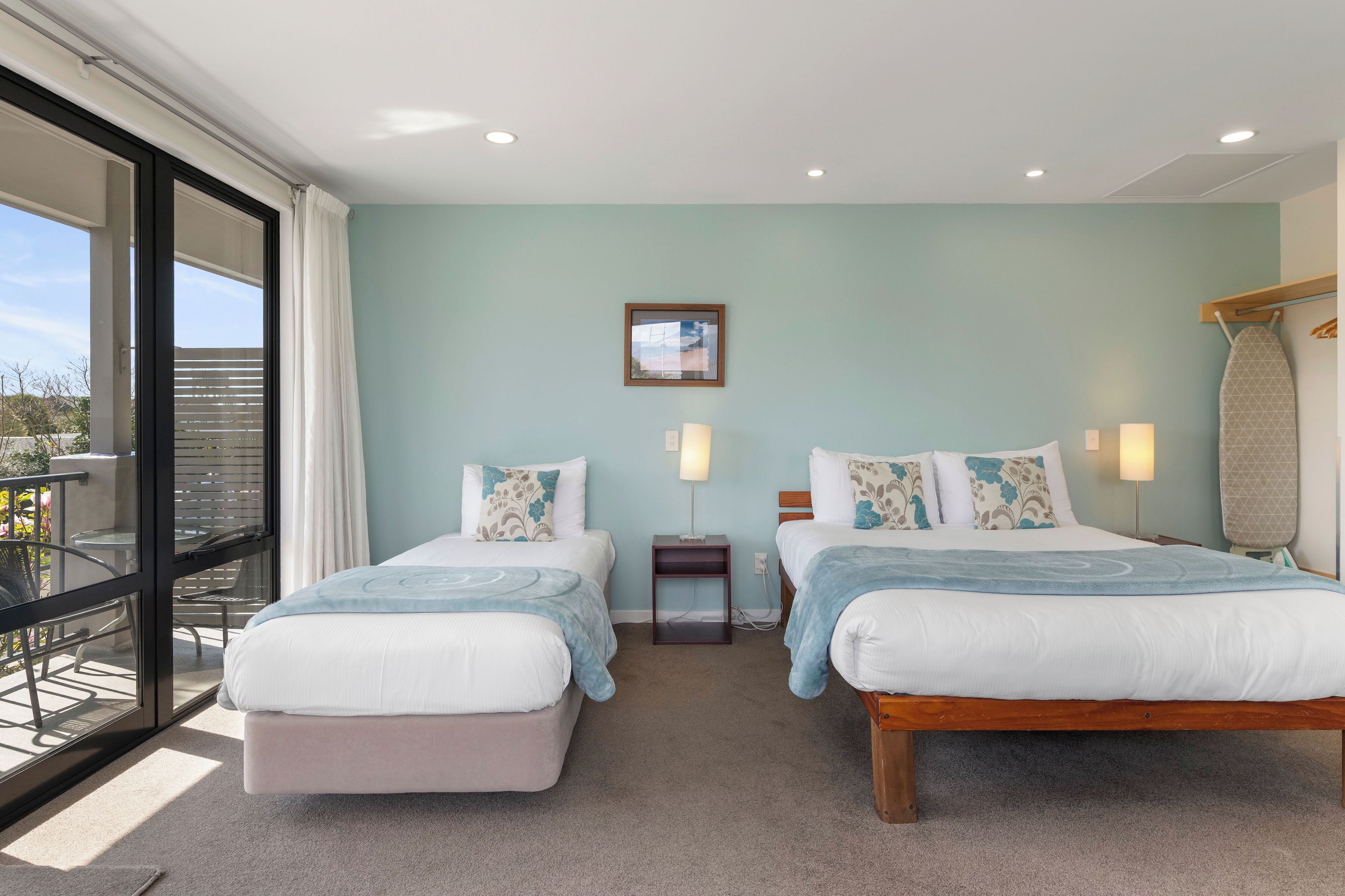 A hotel room with two beds, a balcony, and a view of the outdoors.