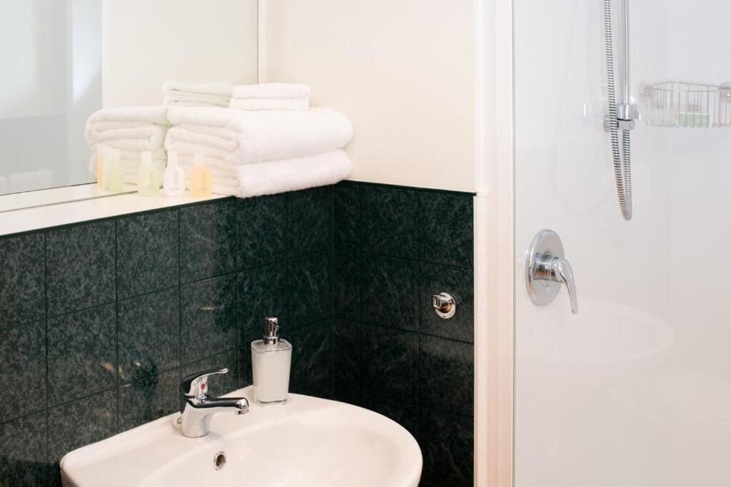 Ein Badezimmer mit Waschbecken, Spiegel und Dusche. Handtücher liegen auf dem Spiegel gestapelt.
