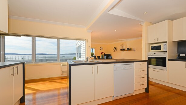 Una cocina moderna con una isla grande, armarios blancos y vista al mar.