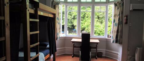 A room with a bunk bed, a desk, and a bay window with curtains.