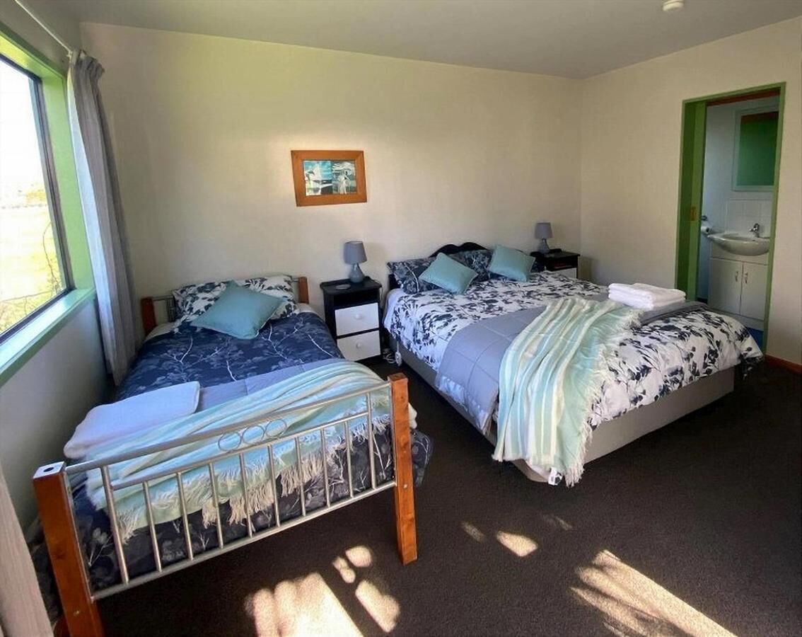A room with two beds, a bedside table with a lamp, a framed picture on the wall, and a green door.