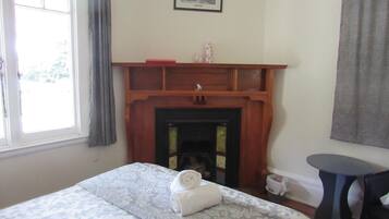 A bedroom with a bed, a fireplace, a small table, and a window with curtains.