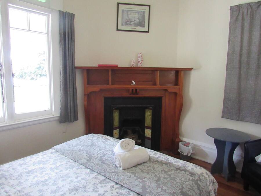 A bedroom with a bed, a fireplace, a small table, and a window with curtains.