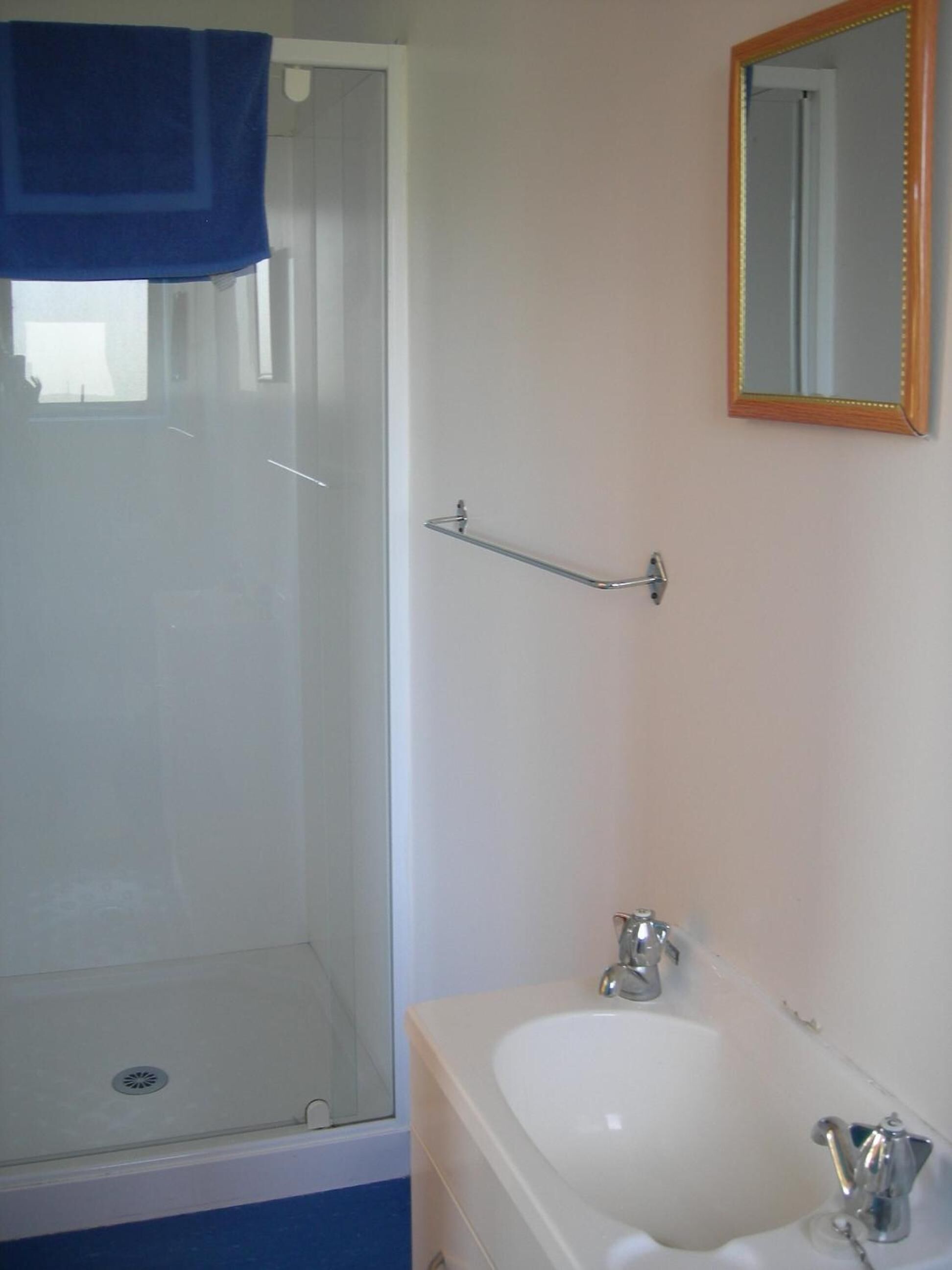 A bathroom with a shower, a sink, a mirror, and a towel rack.