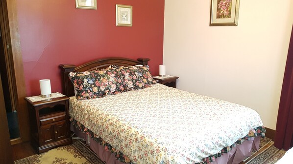 A bedroom with a floral bedspread, a wooden headboard, two bedside tables with lamps, and a nightstand with a lamp.