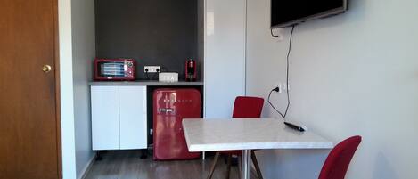 A compact kitchen with a white fridge, a red coffee maker, and a red chair at a table.