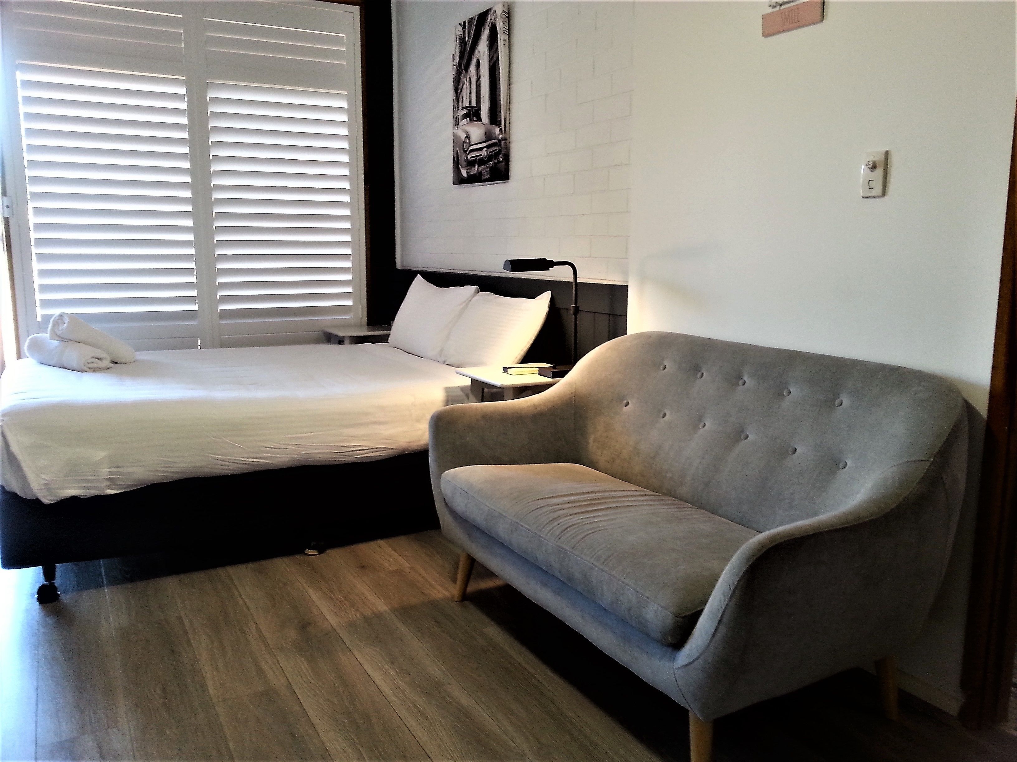 A bedroom with a bed, a grey sofa, a bedside table, and a wall-mounted lamp.