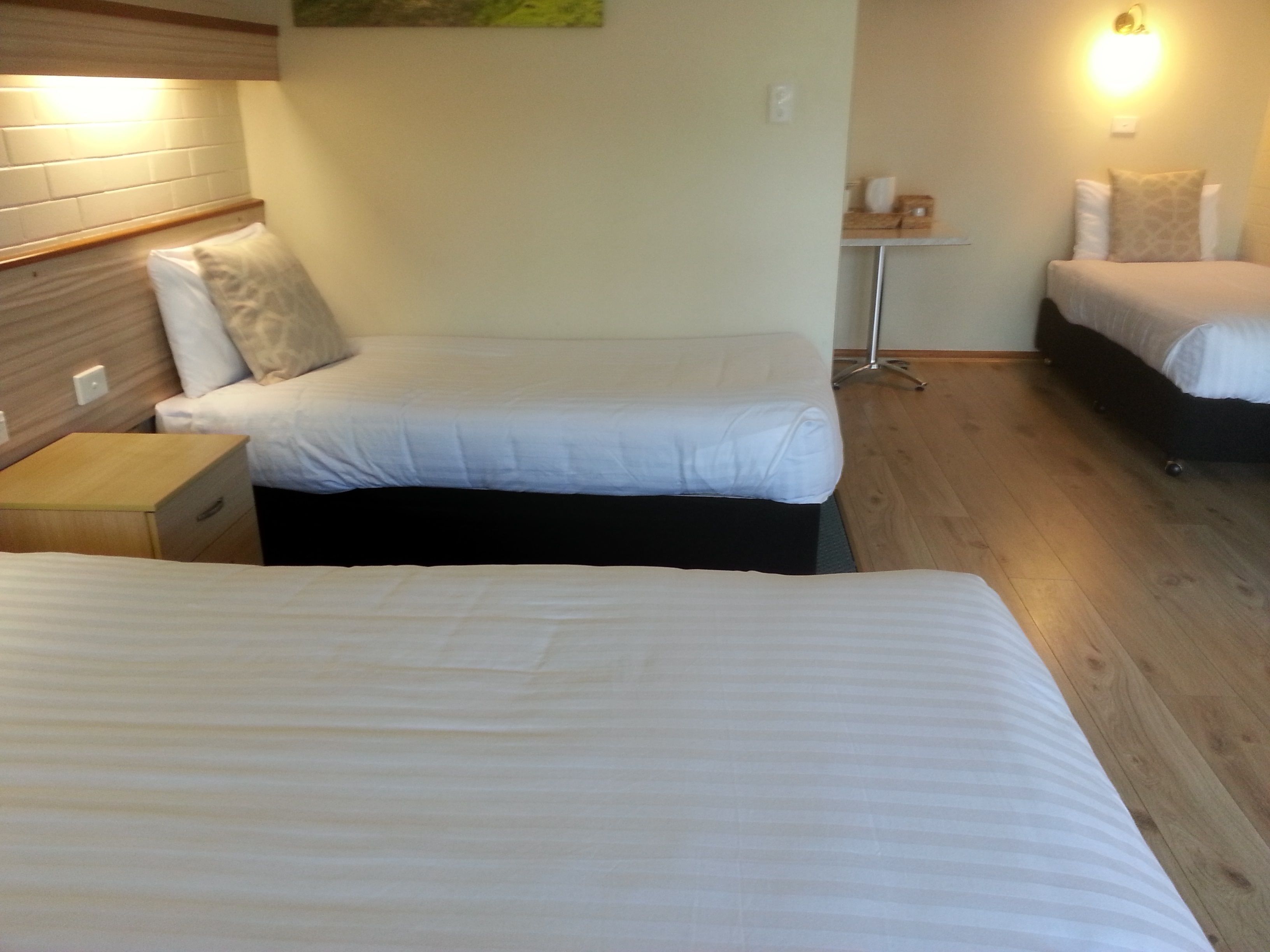 Habitación de hotel con dos camas, una mesita de noche, una pequeña mesa con lámpara y una lámpara de pared.