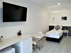 A hotel room with a bed, a desk, a chair, a TV, and a small bedside table. - Kurri Motor Inn (Kurri Kurri)