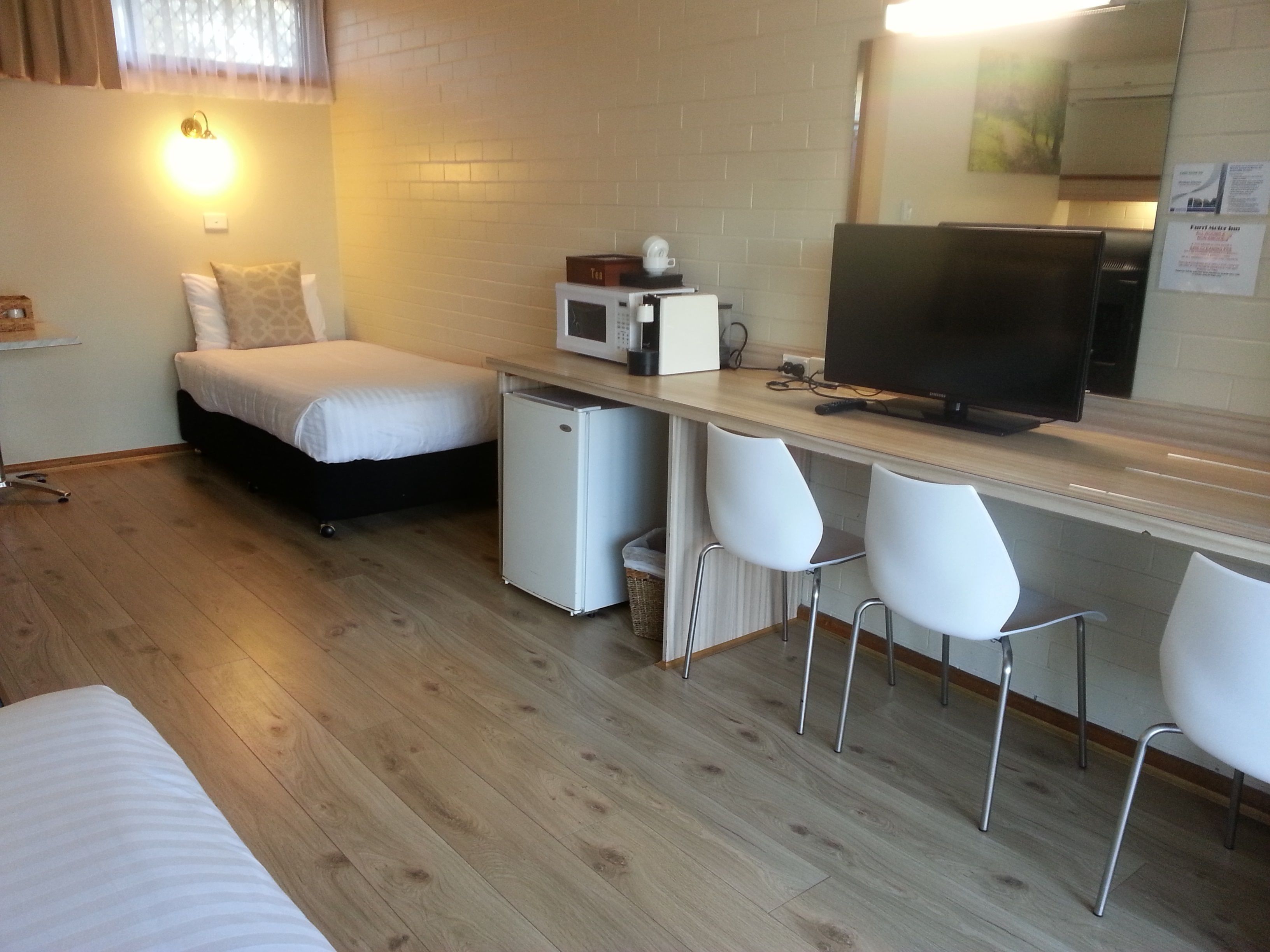 Habitación compacta con cama, un refrigerador pequeño, microondas, televisión y una zona de bar con sillas.
