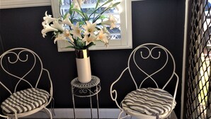A room with two white chairs with heart-shaped backs, a white vase with white flowers, and a window with a view of buildings. - Kurri Motor Inn (Kurri Kurri)