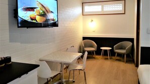 A modern dining area with a flat-screen TV displaying a food advertisement, a white table with four chairs, and a small round table with two chairs. - Kurri Motor Inn (Kurri Kurri)