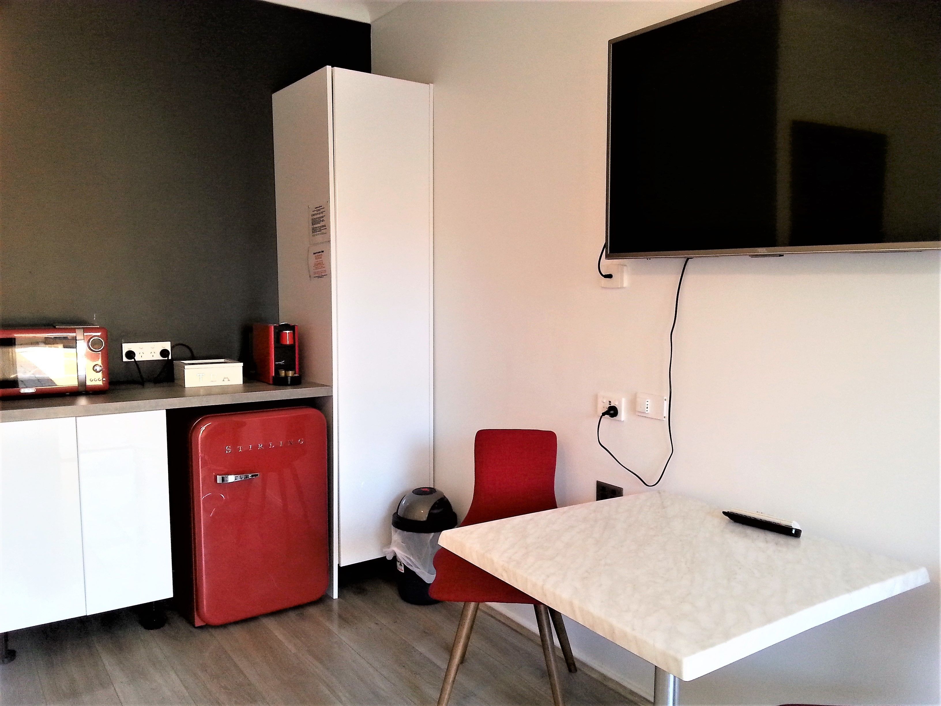 A compact kitchen with a microwave, coffee maker, and a red refrigerator.