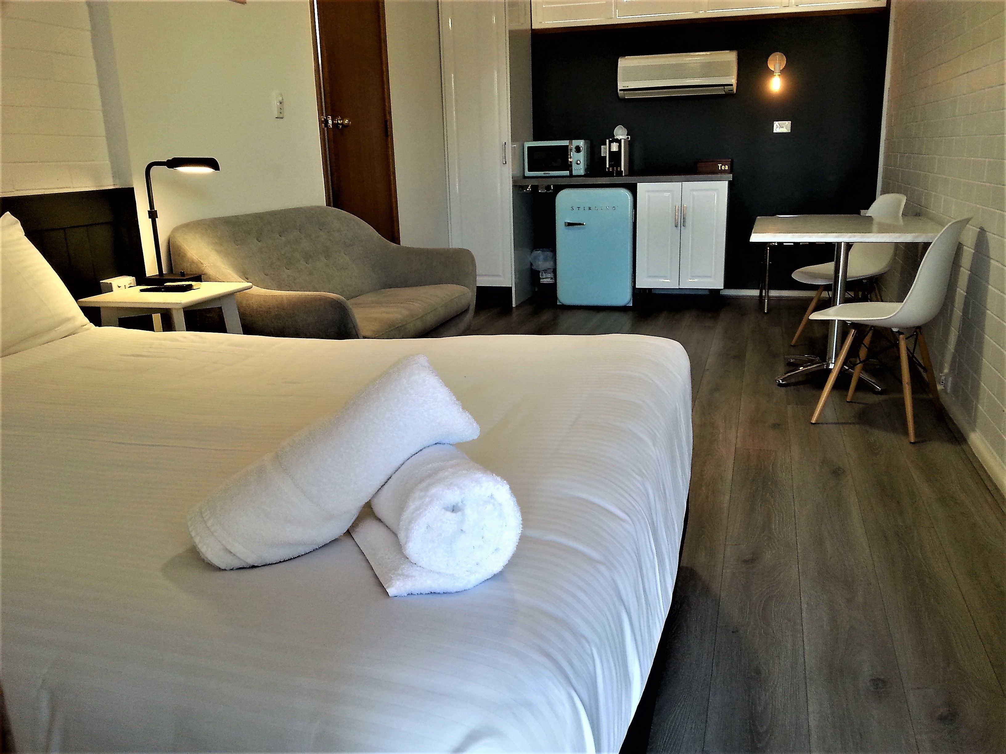 A hotel room with a bed, a chair, a desk, and a kitchenette.