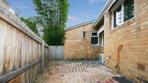 A brick patio with a wooden fence, a brick wall, and a window. - Lisson Holiday Rental (Hawthorn)