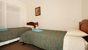 A room with two single beds, a wooden headboard, a small bedside table with a vase of flowers, and a framed picture on the wall. - Lisson Holiday Rental (Hawthorn)
