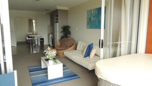 A modern living room with a sofa, a coffee table, and a dining area in the background.