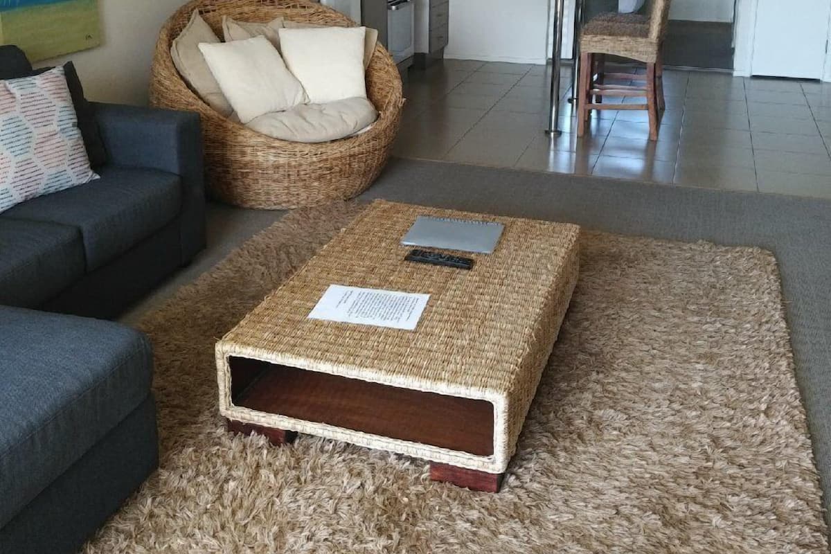 Uma sala de estar com sofá, uma poltrona de vime, mesa de centro e tapete.