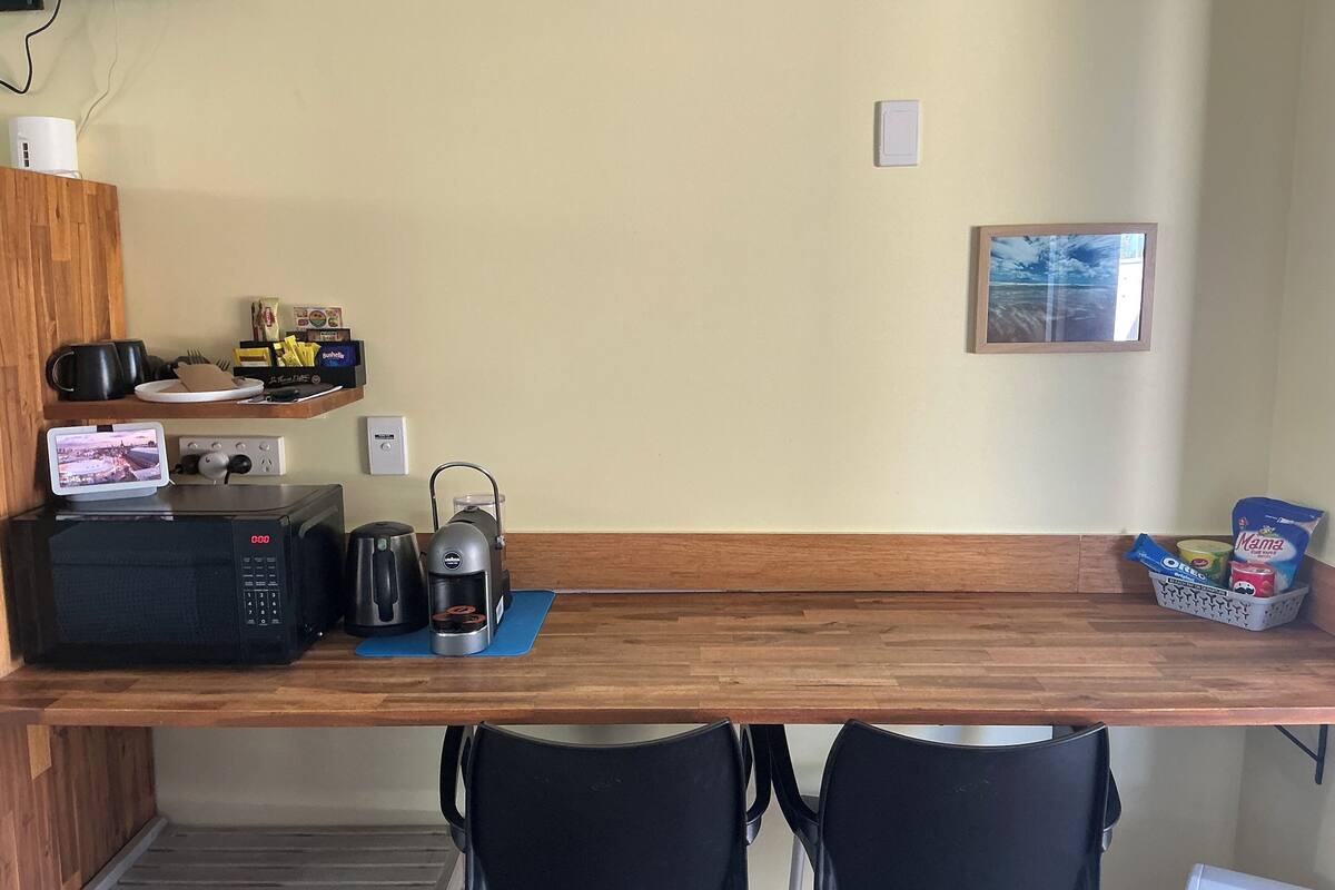 Una kitchenette equipada con microondas, cafetera y tostadora. Hay dos sillas y una mesita.