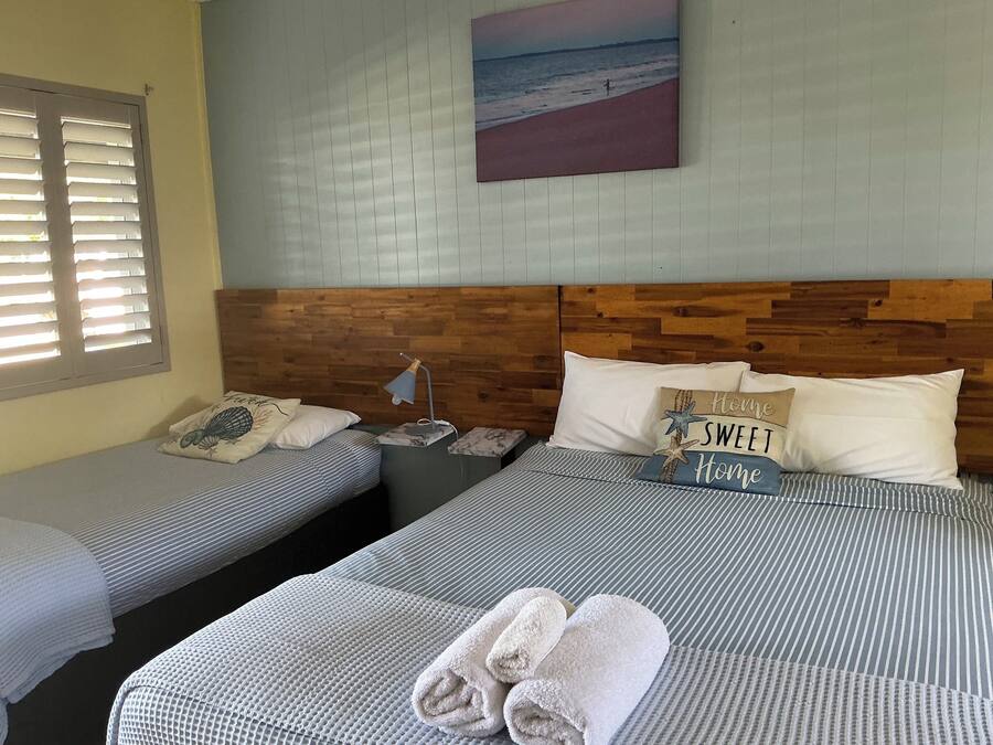 Ein Hotelzimmer mit zwei Betten, einem Holzkopfende, einem Strandgemälde und einem Nachttisch mit Lampe.