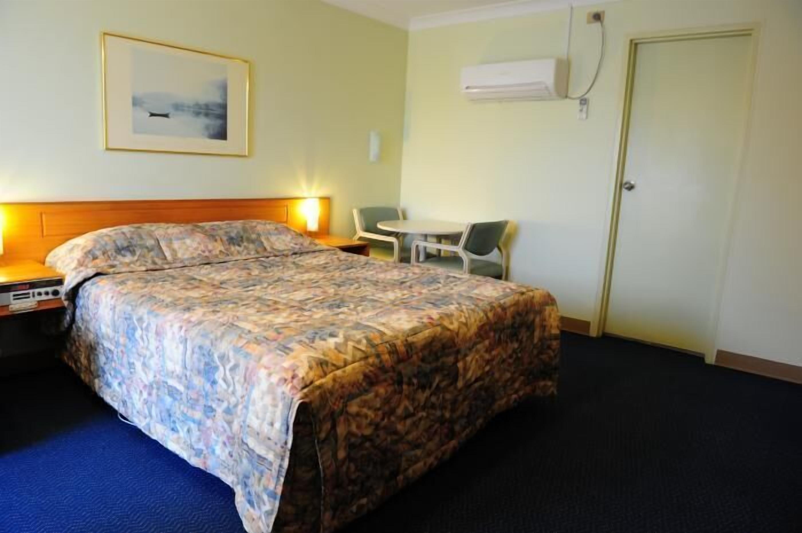 Una camera d'albergo con un letto, un comodino, una sedia e un piccolo tavolo.