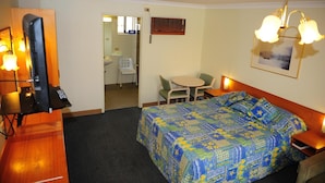 Quarto de hotel com cama, escrivaninha com computador, cadeira, mesa pequena e um quadro na parede.