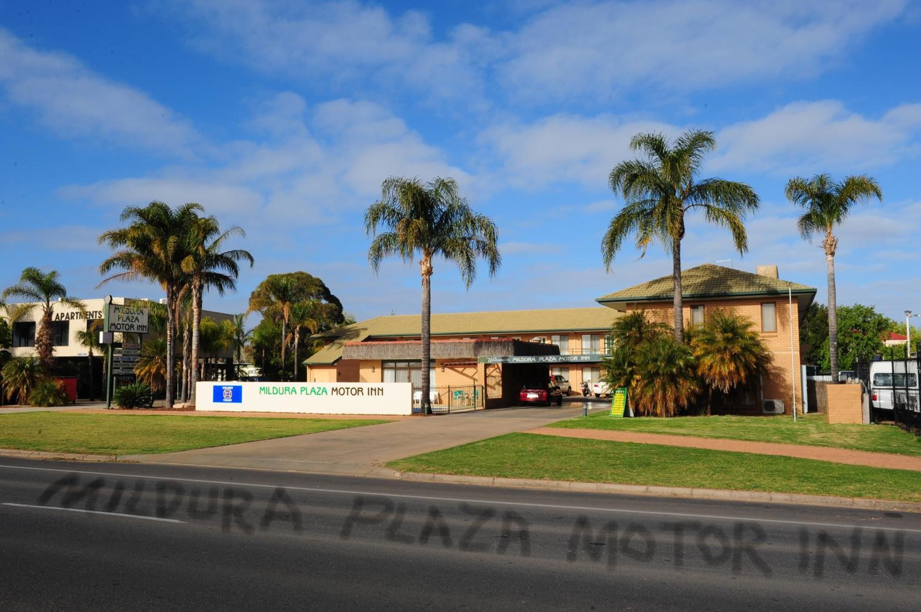 A building with a sign for Mildura Plaza Motor Inn, surrounded by palm trees and a clear sky.