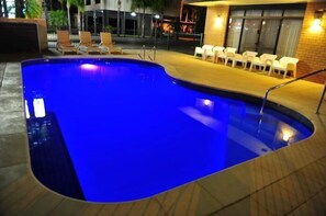 A swimming pool with a blue tint, surrounded by a tiled deck and white plastic chairs. - Mildura Plaza Motor Inn (Mildura)
