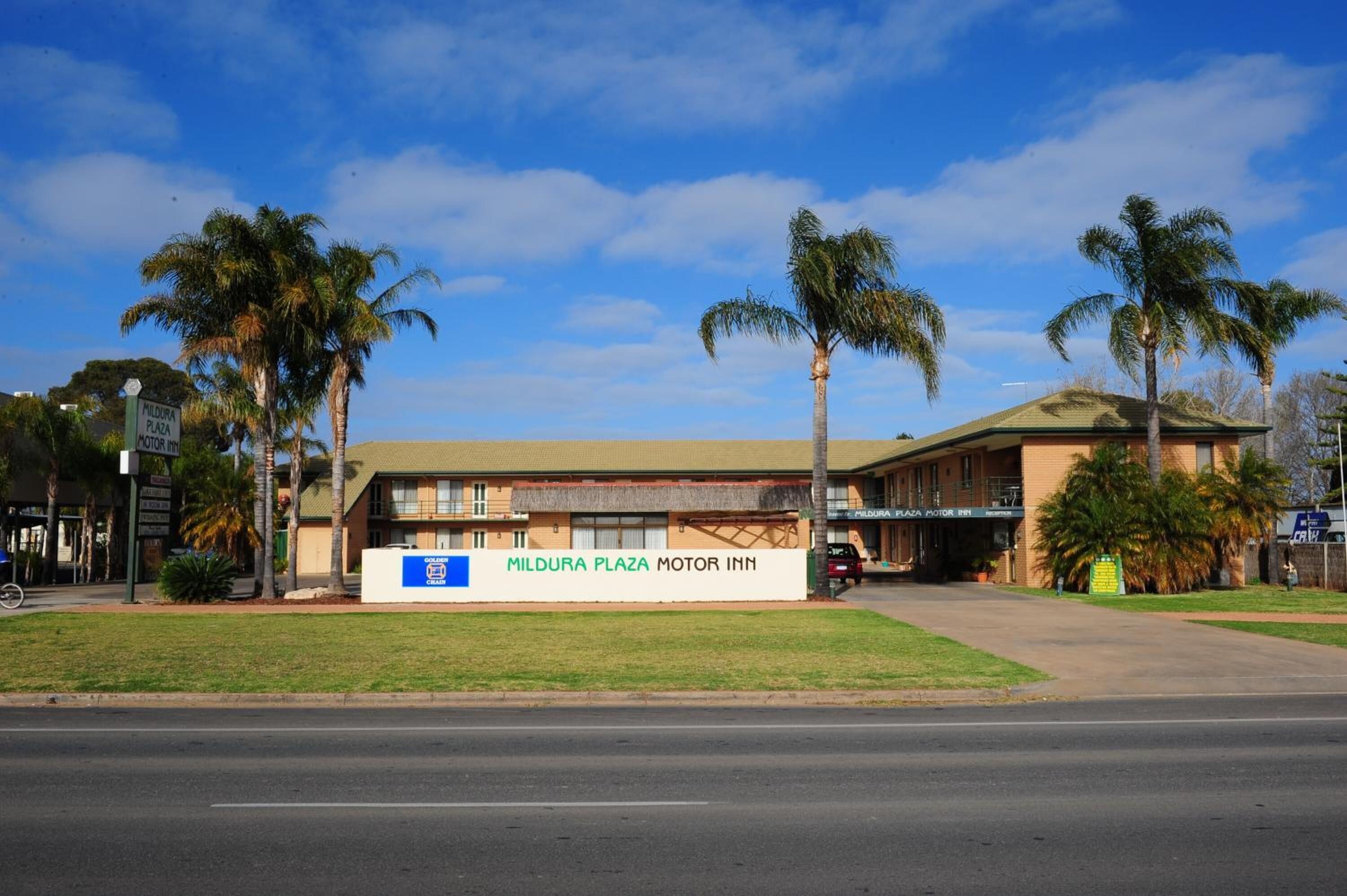 A building with a sign reading "Mildura Plaza Motor Inn" and palm trees in front.