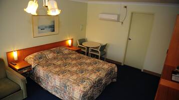 A hotel room with a bed, bedside table, lamp, chair, and a small table with a chair.