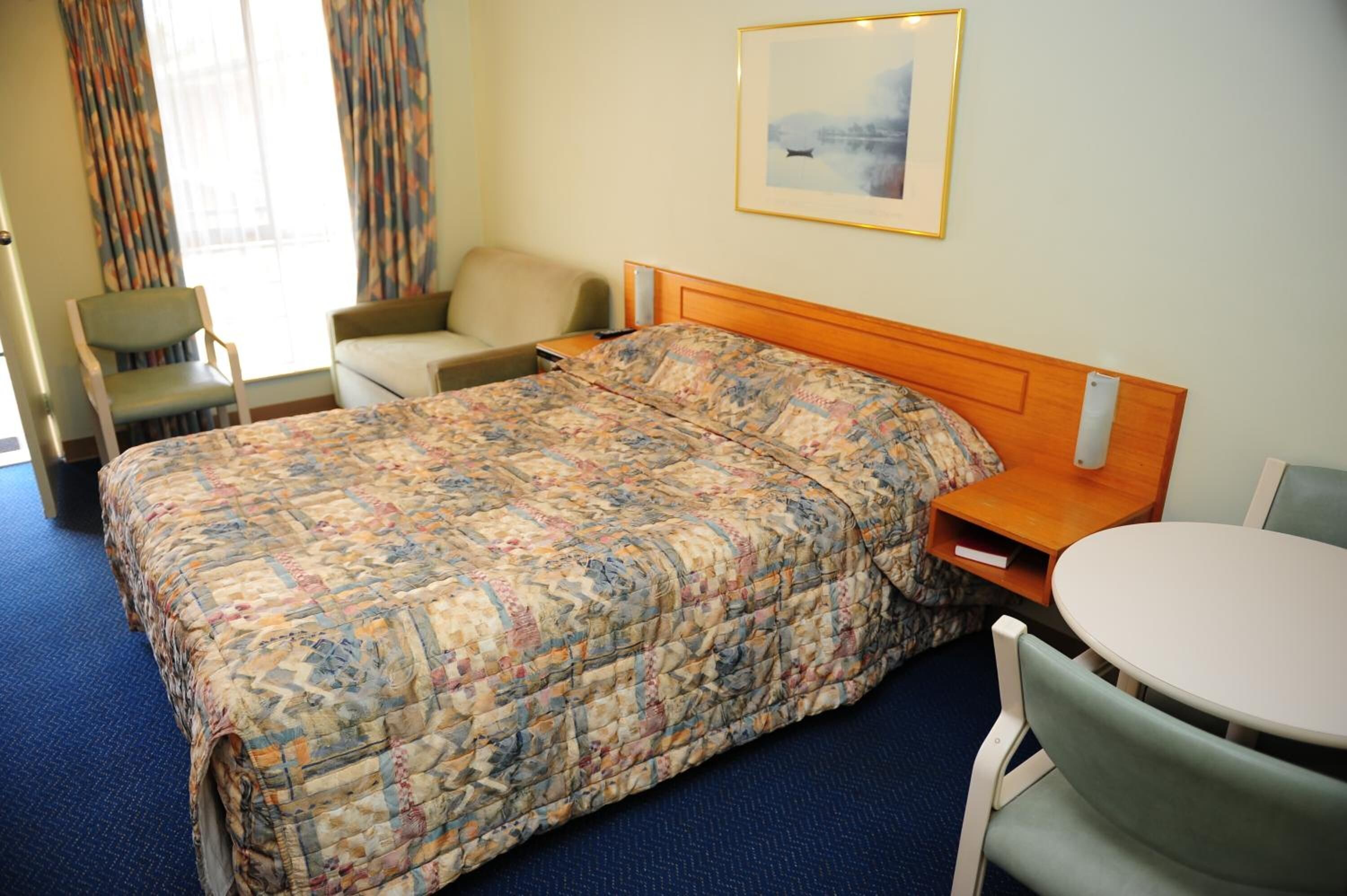 Une chambre d’hôtel avec un lit, une chaise, une petite table et un tableau au mur.