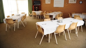 Uma sala de conferências com várias mesas e cadeiras, uma lousa e um relógio na parede.