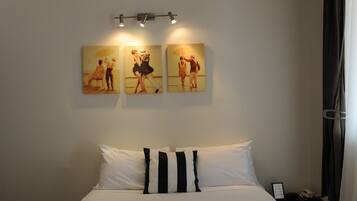 A hotel room with a large bed, two wall-mounted light fixtures, and three paintings depicting dancers.