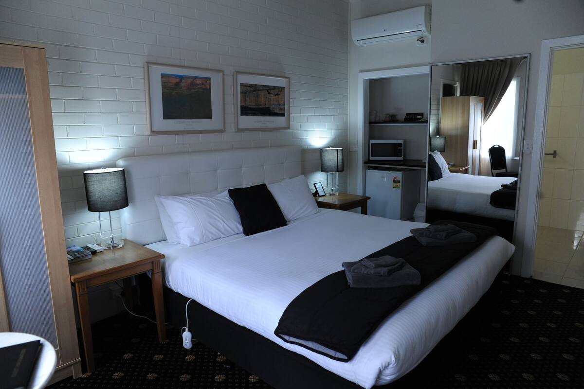 A hotel room with a large bed, a nightstand, a lamp, a mirror, and a wardrobe.