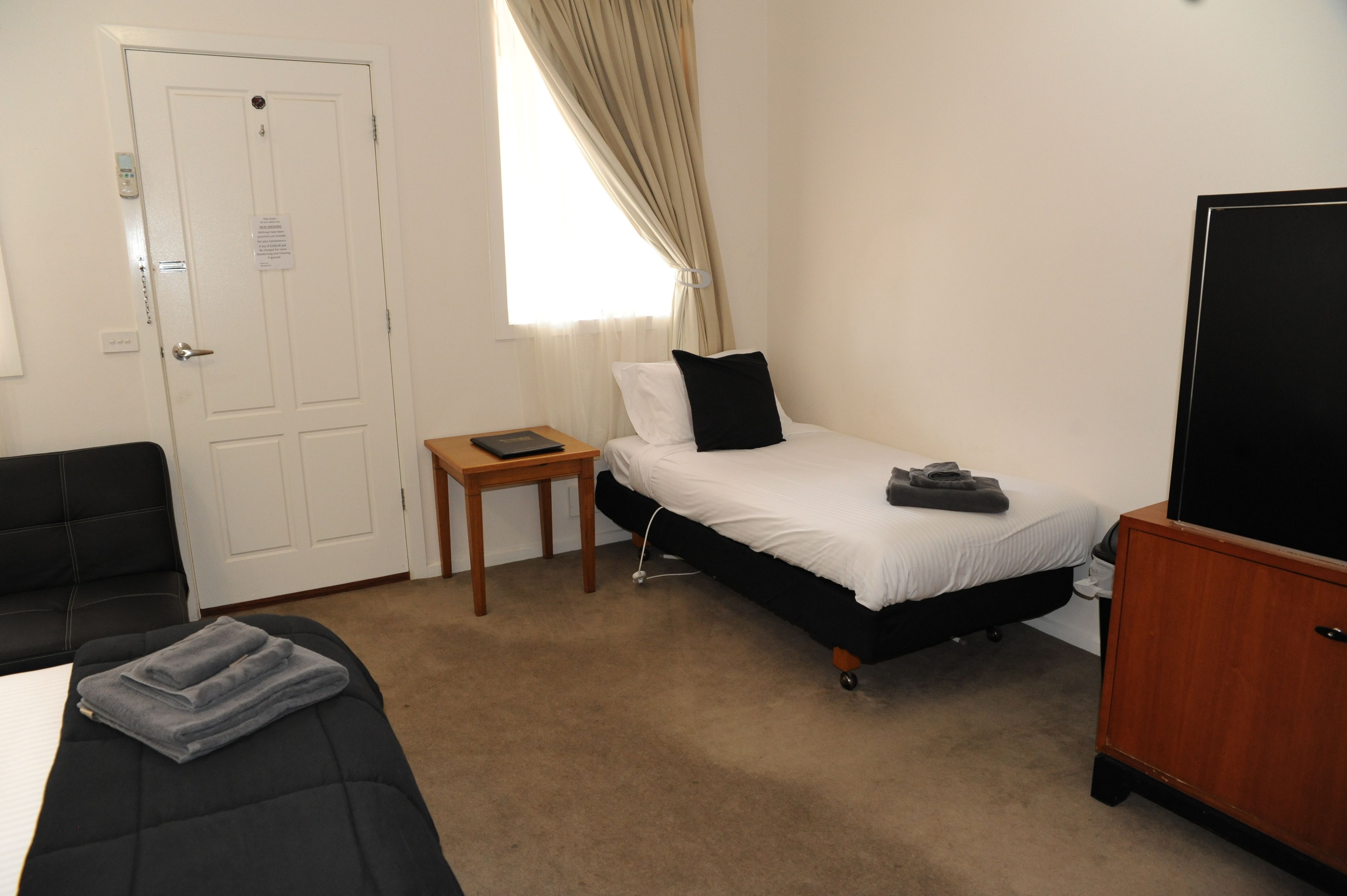 A small, tidy room with a single bed, a small table, a chair, and a TV.