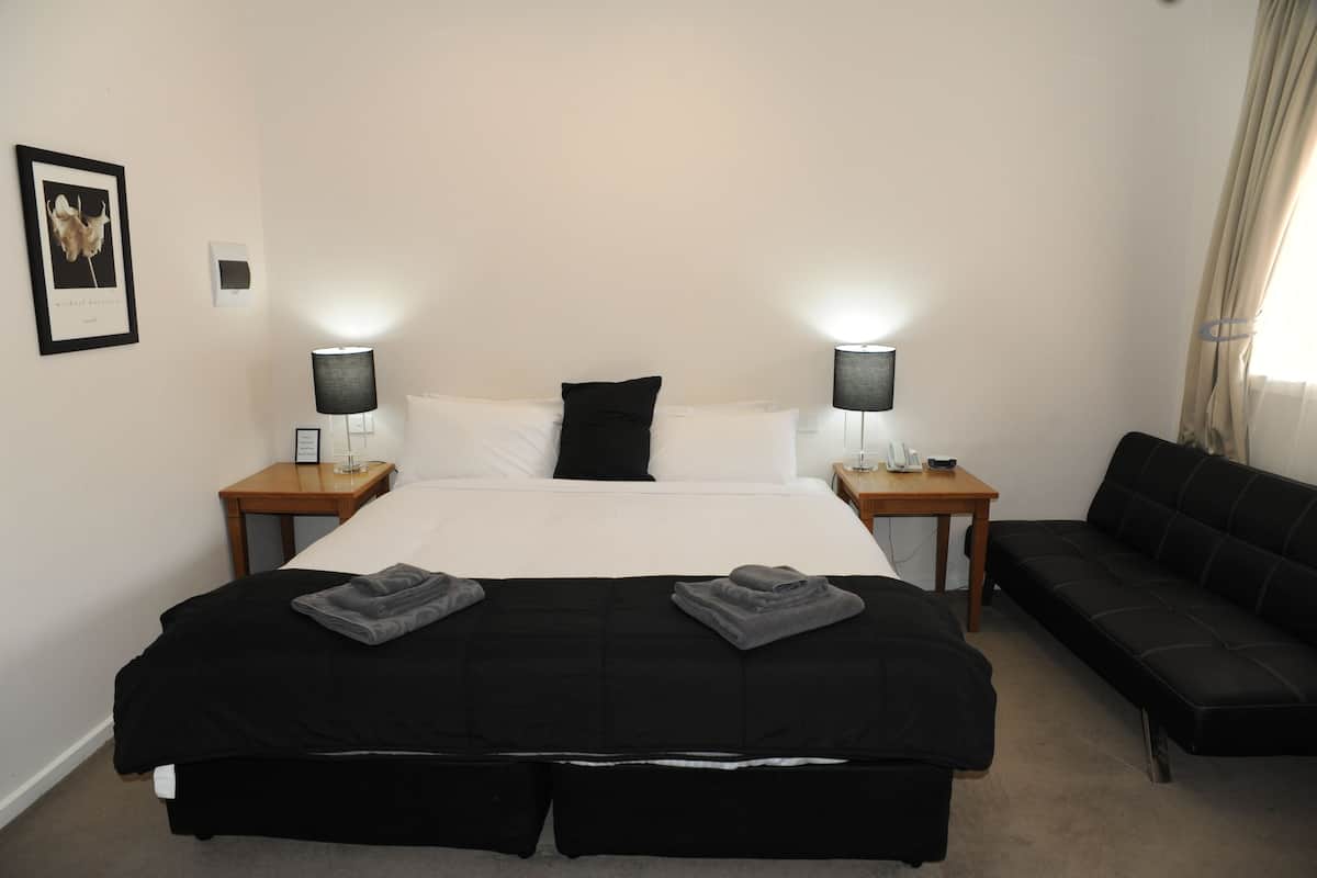 A hotel room with a large bed, two bedside tables with lamps, a black sofa, and a framed picture on the wall.