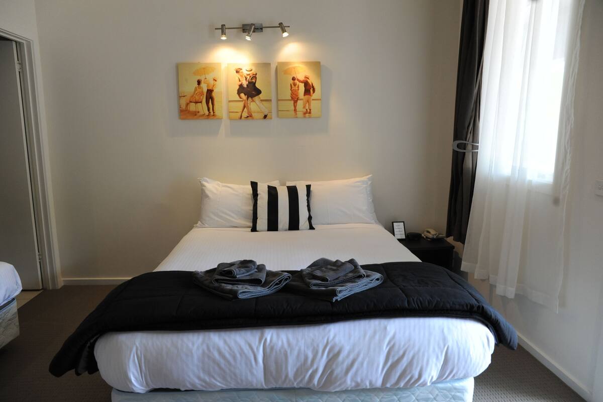 A hotel room with a large bed, black and white striped pillows, a black throw blanket, and two paintings on the wall.
