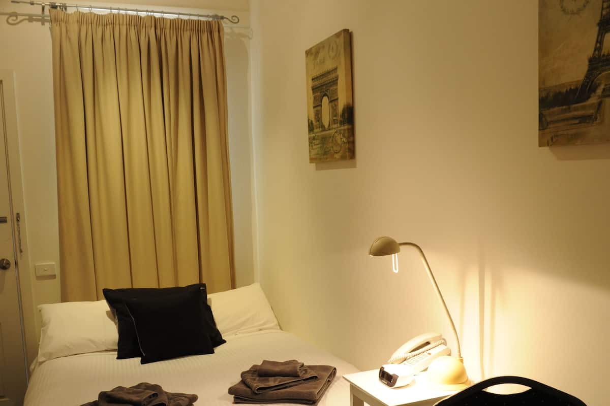 A hotel room with a bed, a desk with a lamp, a chair, and a small table.