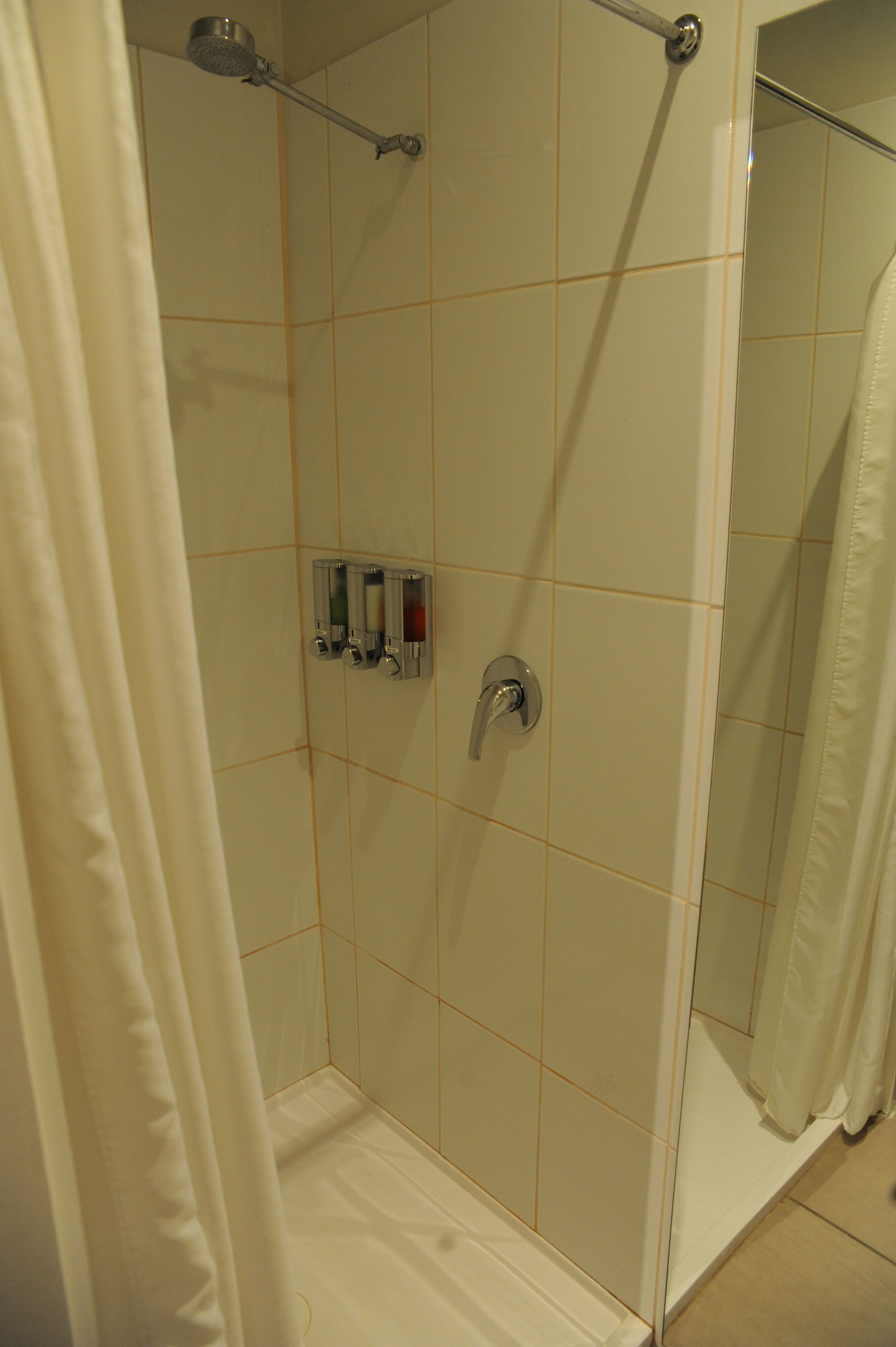 A glass-enclosed shower with a handheld showerhead, a control panel with multiple buttons, and a white shower curtain.