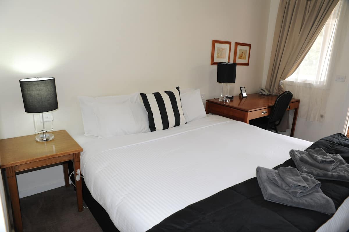 A hotel room with a bed, a desk, a chair, a lamp, and a window with curtains.