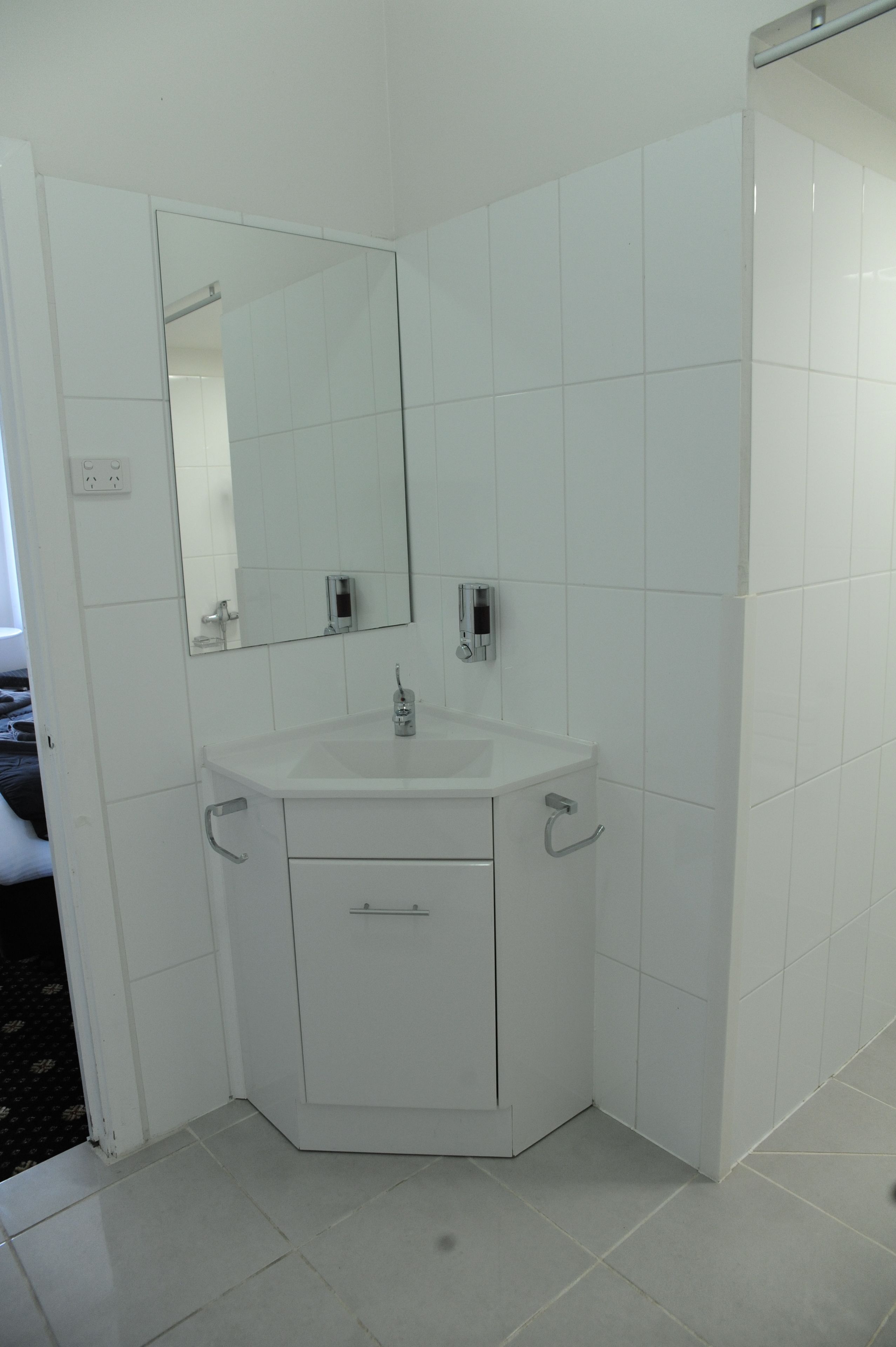 A corner bathroom with a white sink, mirror, and cabinet.