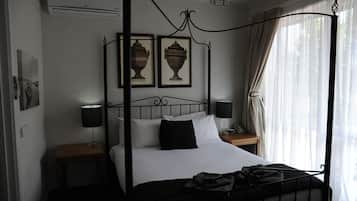 Una cama con dosel, dos mesitas de noche, una lámpara en cada una y un cuadro enmarcado sobre la cama.