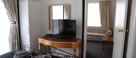 Et hotelværelse med en seng, et fjernsyn på en trækommode, et spejl og en sofa i baggrunden.