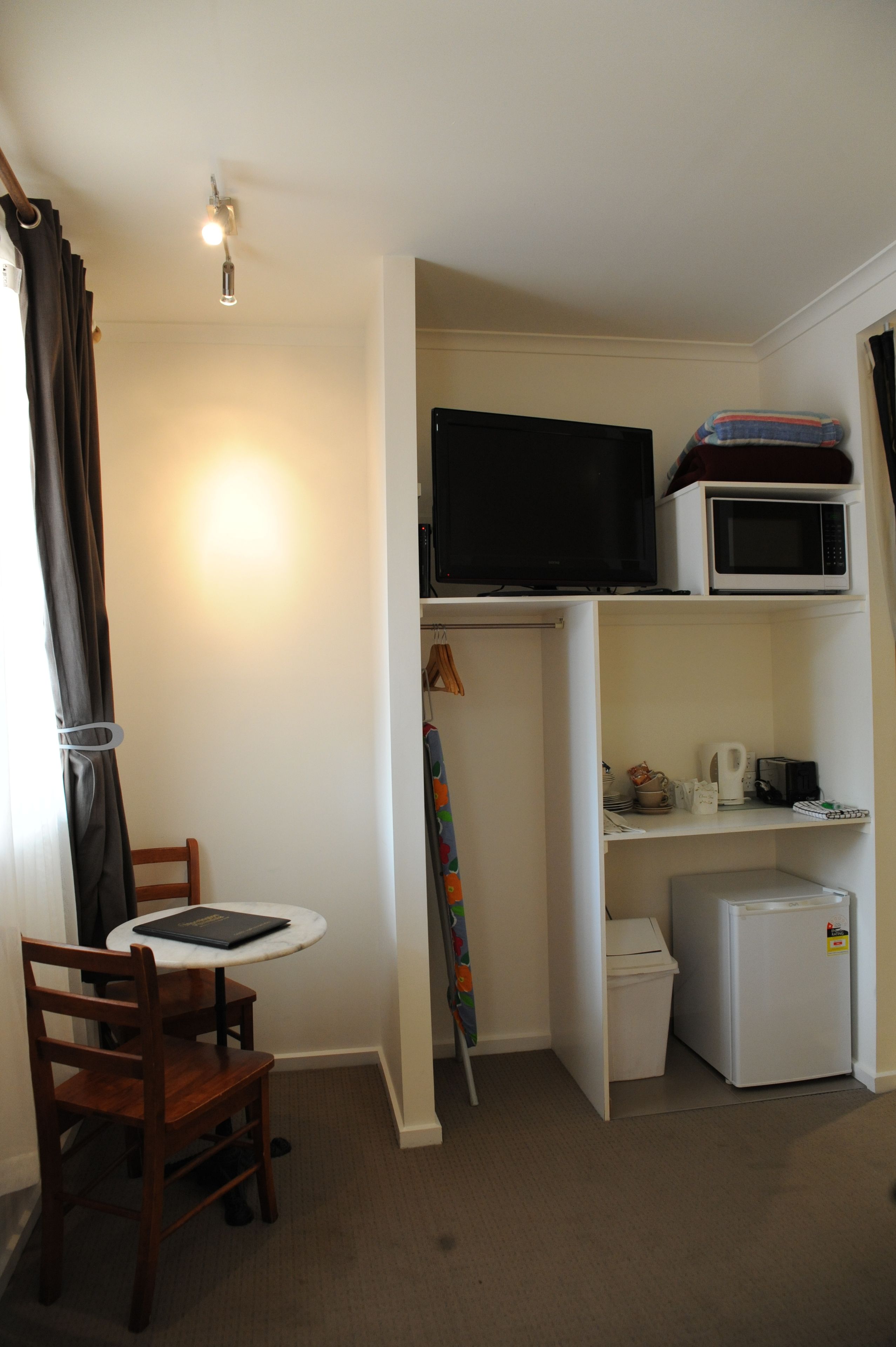 Una habitación compacta con una mesa de comedor, una silla, televisor, microondas y refrigerador.