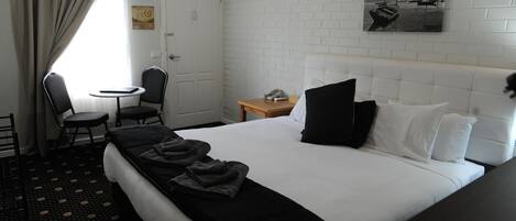 A hotel room with a bed, a desk, a chair, and a small table.