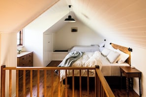 A bedroom with a sloped ceiling, a bed with pillows, a nightstand, a dresser, and a window. - Daisy Bank Cottages (Richmond)
