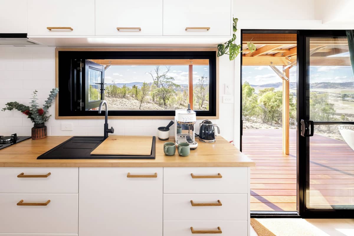 A modern kitchen with a large window, wooden countertop, and white cabinets.